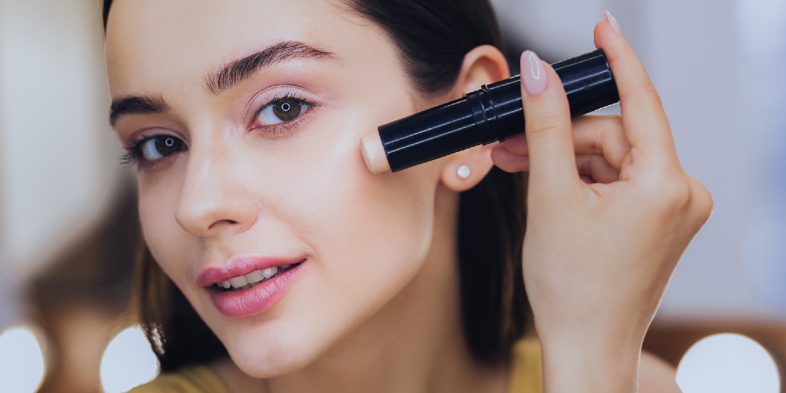 concealer-vs-foundation the-independence Charming woman using concealer stick while putting makeup on