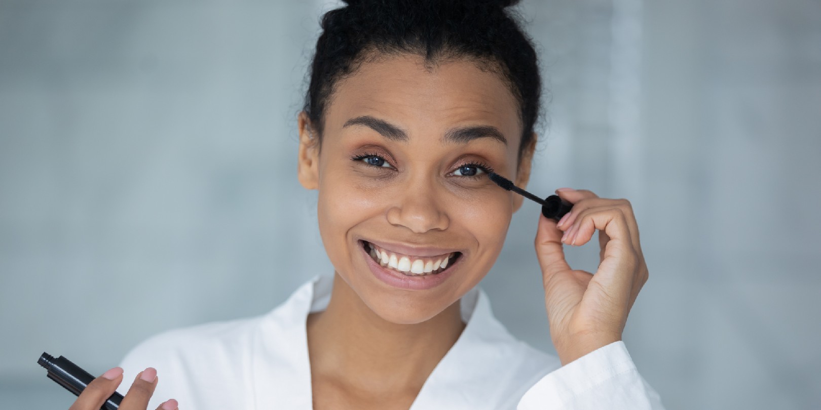 remove-waterproof-mascara the-independence Head shot portrait african woman holding black tube applying volumizing mascara