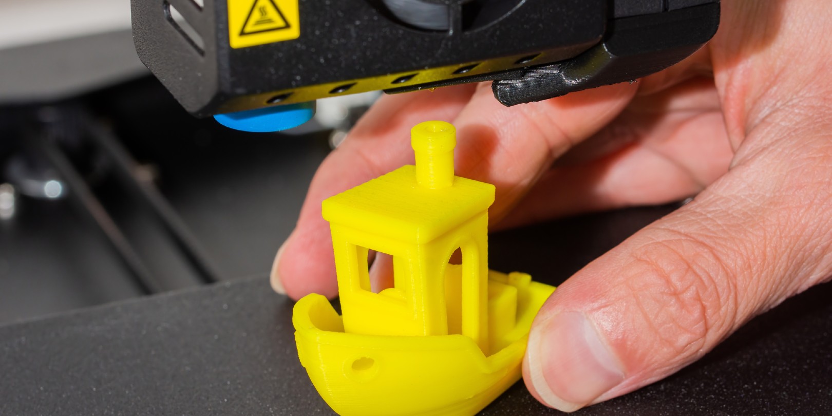 fdm-3d-printing the-independence Close-up of man hands taking finished 3D printed model of yellow PLA ship