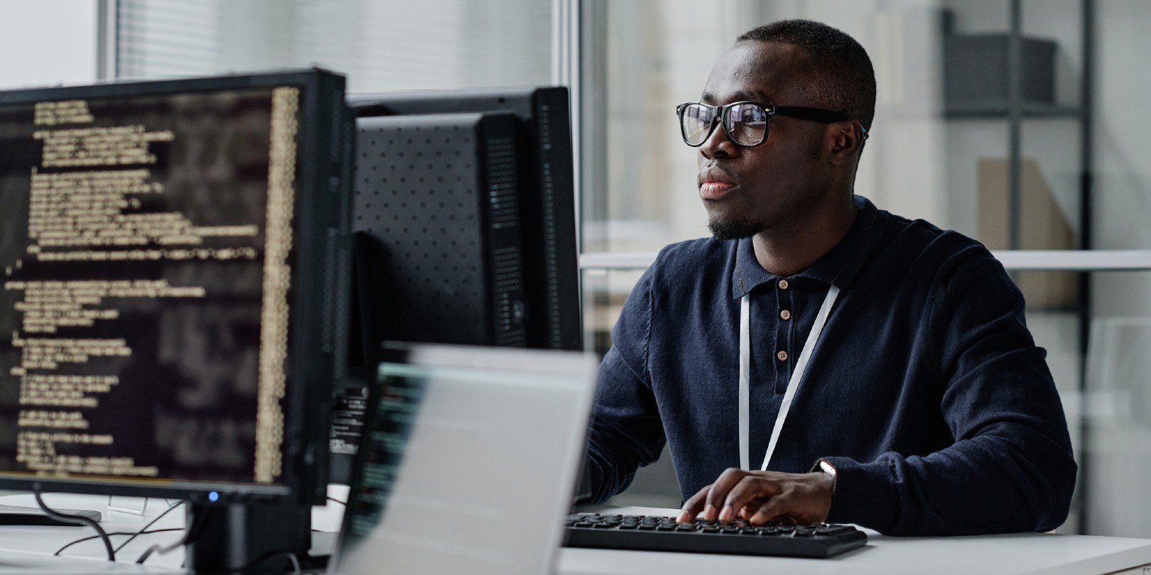 how-to-get-into-cyber-security the-independence African American young developer in eyeglasses concentrating on his online work on computer sitting at workplace