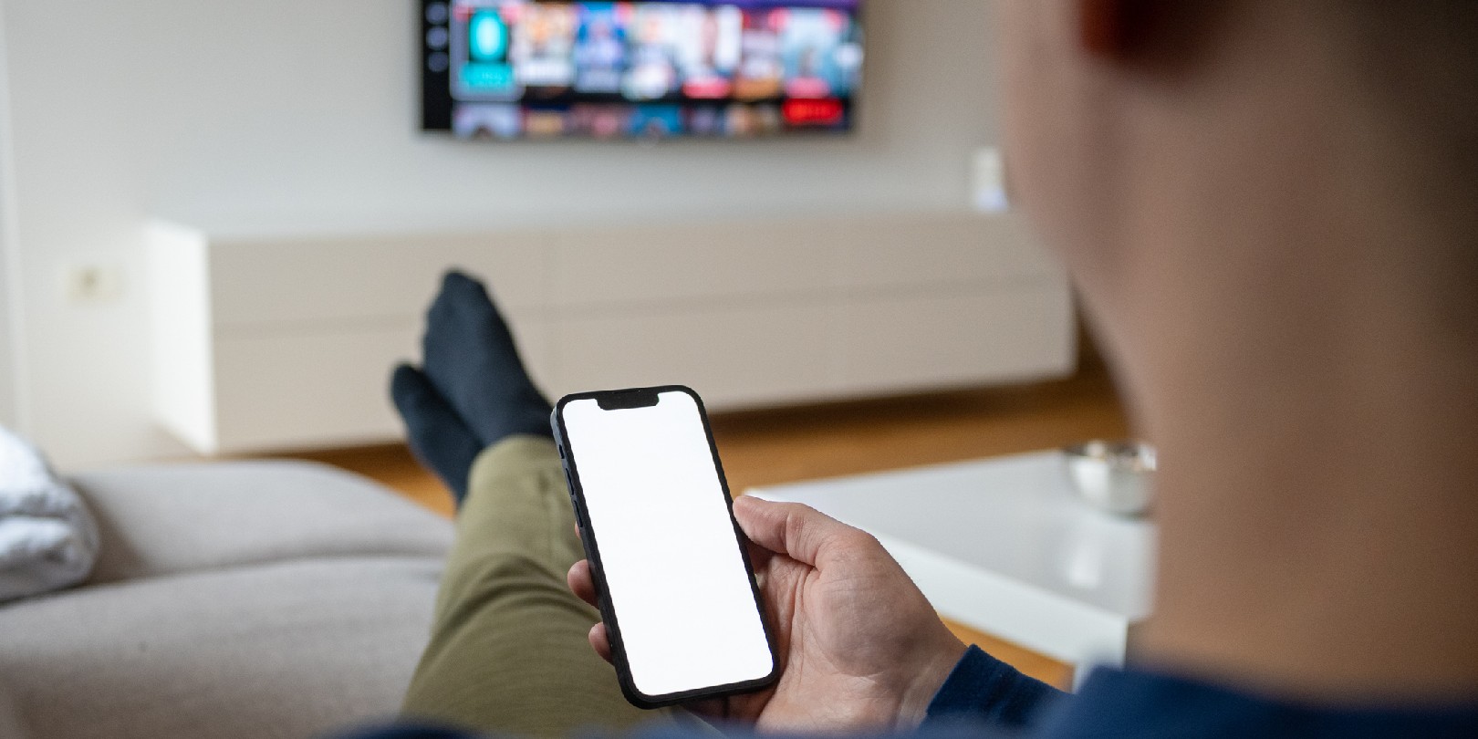 mirror-iphone-on-tv the-independence Over the shoulder view of a caucasian man holding a smart phone with a white screen while watching TV.