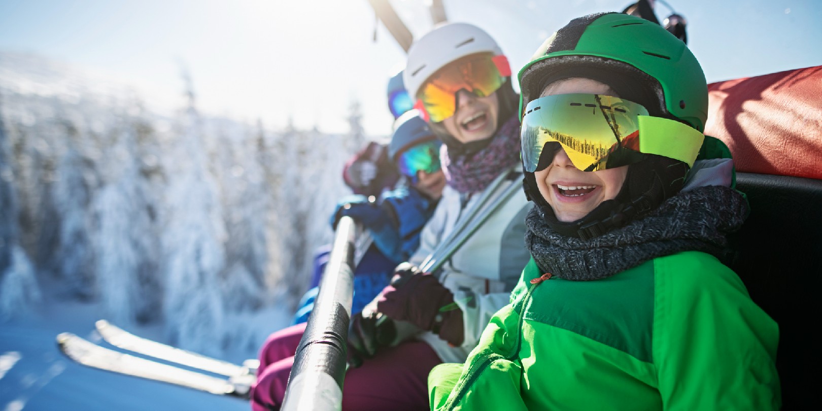ski-trip-packing-list the-independence Mother skiing with kids on a sunny winter day. Family is sitting on chairlift cheering at the camera