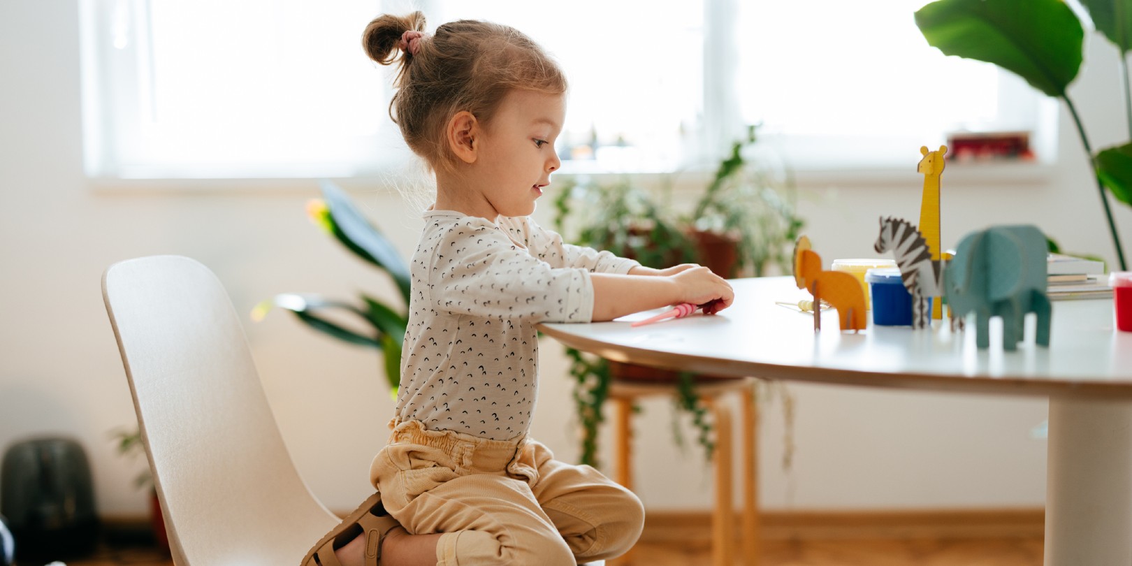 small-nursery-ideas the-independence Cute little girl is crouching on the chair playing with paper animals that are on the table.
