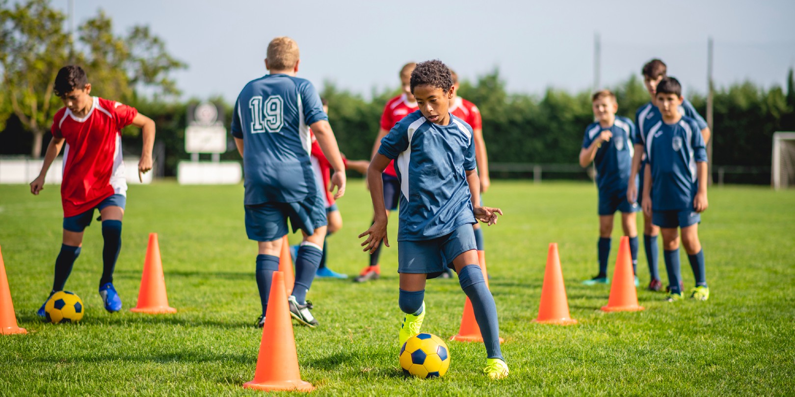 football-drills-for-beginners the-independence Young male athletes doing dribbling drills around pylons to improve ball control skills.
